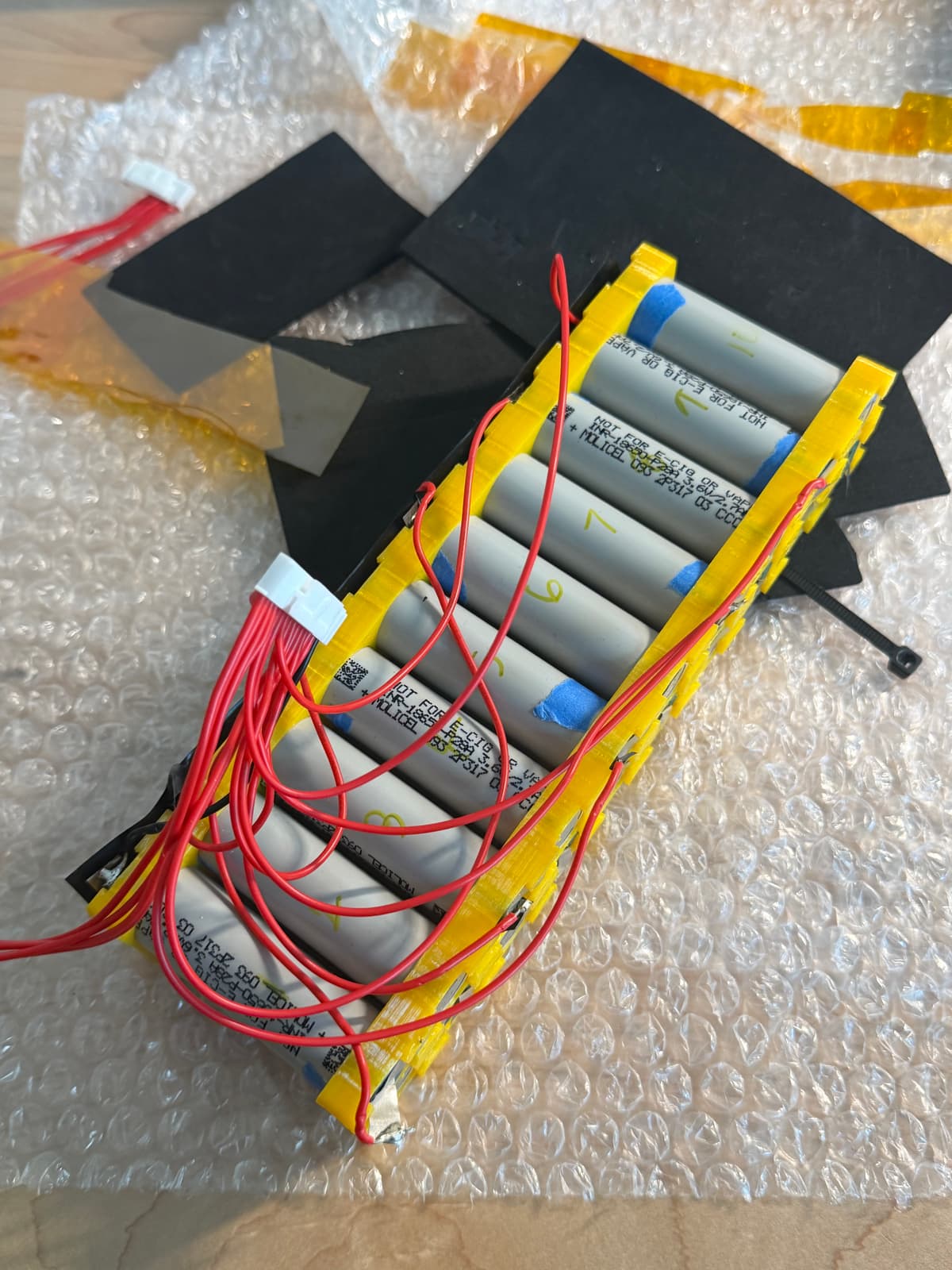 A part-assembled lithium battery module: cylindrical cells held in a printed frame with balance leads routed to a connector.